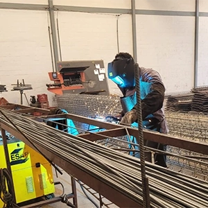 imagem de um soldador realizando o trabalho de solda, protegido com máscara, avental e luvas